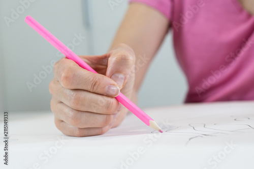 Obraz na płótnie Macro shot of a person's hand holding a bright pink pencil, carefully drawing precise lines on paper for art class, back to school homework, or design project