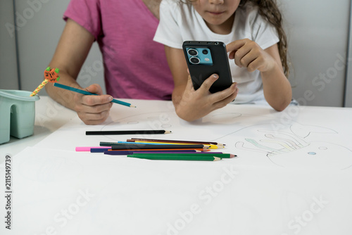 фотографія A mother sitting next to her left-handed child as the child operates a smartphone during a creative drawing and study session