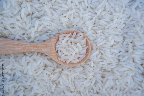 Raw Jasmine rice in a wooden spoon on raw white rice background