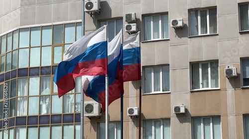 Three Russian flags wave in the wind against the backdrop of a building on a sunny day. The Russian tricolor