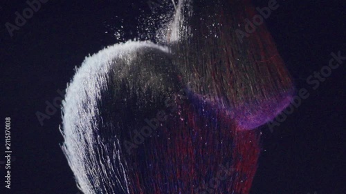 Slow motion shot of vibrant powder being spread. An artistic representation of makeup brush releasing shimmering particles in slow motion against dark backdrop
