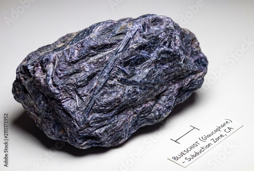 A dark blue schist rock sample with visible foliation and a scale bar for geological reference.