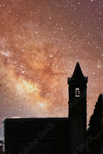 A silhouette of an ancient church and its bell tower stands out against a swirling, star-filled night sky
