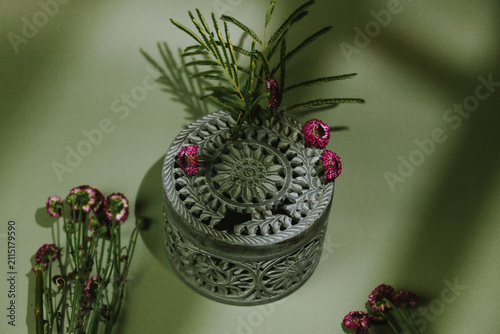 Canvas Print An ornate silver trinket box with a carved circular lid is surrounded by magenta flowers and green foliage, with dramatic botanical shadows crossing the muted green background