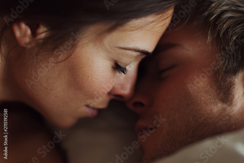 Close up of romantic loving young couple leaning foreheads with eyes closed in bed