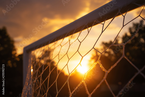 Close up of soccer goal net on a football field during a dramatic golden sunset background