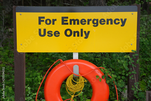 Bright orange life ring with coiled yellow rope hangs beneath a yellow sign reading 