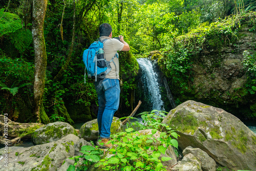 Man backpacking, photographing waterfall in lush forest