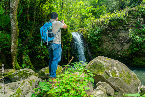 Man hiking and photographing beautiful waterfall in forest