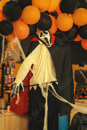 Fotografie Masked Halloween figure stands beneath orange and black balloons with cobweb decor in retail space