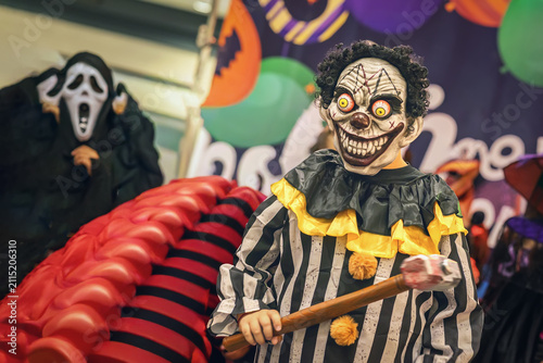 Obraz na płótnie Halloween participant wears clown mask and striped costume while holding prop toy hammer, public event