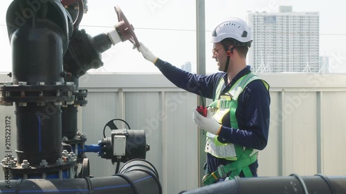 Two industrial technicians in safety helmets and vests adjusting a large valve on a heavy pipeline system at an industrial facility.