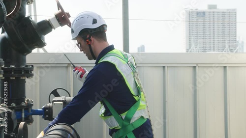 Two industrial technicians in safety helmets and vests adjusting a large valve on a heavy pipeline system at an industrial facility.