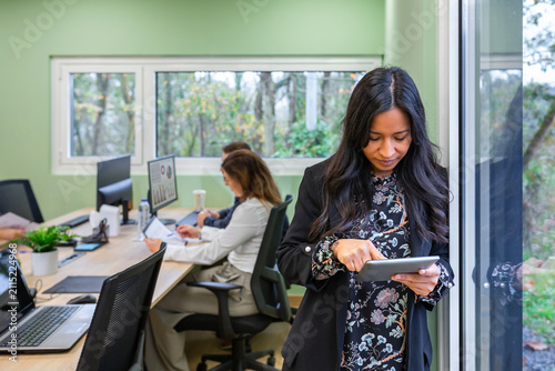 Portrait of businesswoman looking digital content on a tablet, representing connection, smart work and professional mobile technology while colleagues works in background. Copy space available on left