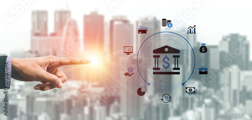 Canvas Print Business concepts with hand pointing at virtual bank icon surrounded by financial symbols and skyscrapers in a contemporary urban landscape backdrop