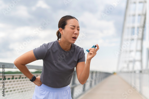 Asian woman suffering asthma attack using inhaler during exercise