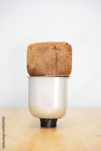 Freshly baked bread loaf cooling on metallic breadmaker container pan standing on wooden table bright modern kitchen interior rustic homemade healthy organic culinary baking concept