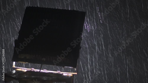 intense rainfall captured at night with raindrops brightly illuminated by a backlit floodlight, creating dramatic streaks against a dark sky with strong atmospheric mood and copy space