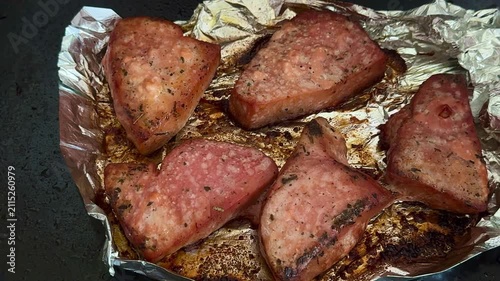 Grilled meat pieces on aluminum foil with visible seasoning and grill marks, arranged in a close-up view showcasing the cooking process and texture of the food