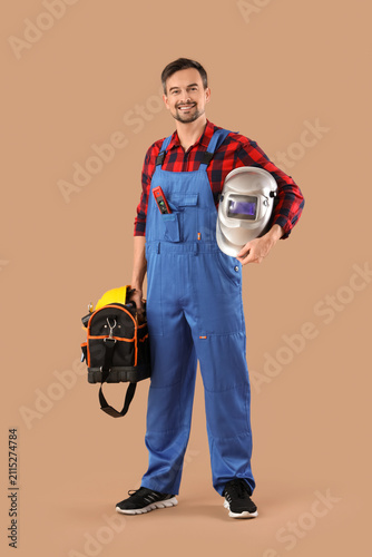Male technician with welding mask and  bag of tools on beige background