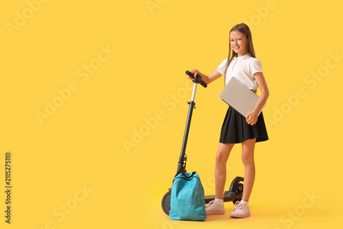 Cute schoolgirl with laptop and electric scooter on yellow background