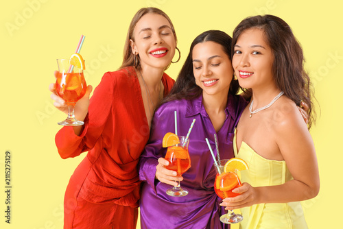 Beautiful young women with aperol spritz cocktail on yellow background