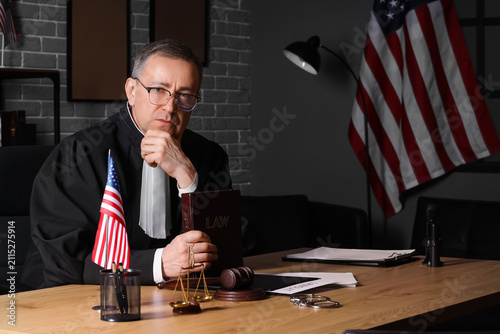 Mature judge with law book sitting at table in office