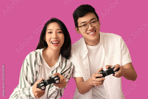 Young Asian friends playing video game on violet background
