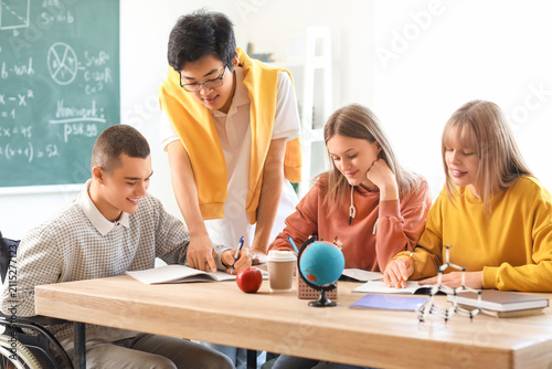 Group of teenage students with boy in wheelchair studying at school