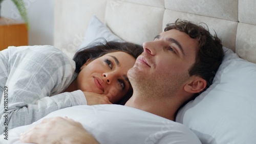 Konstfotografi Happy young Caucasian couple lying together on bed bedroom cuddling talking love