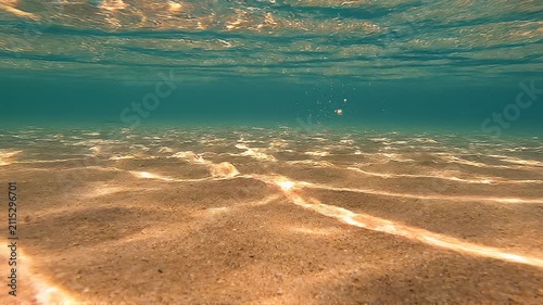 Underwater view of a sandy seabed with sunlight reflections and crystal blue water