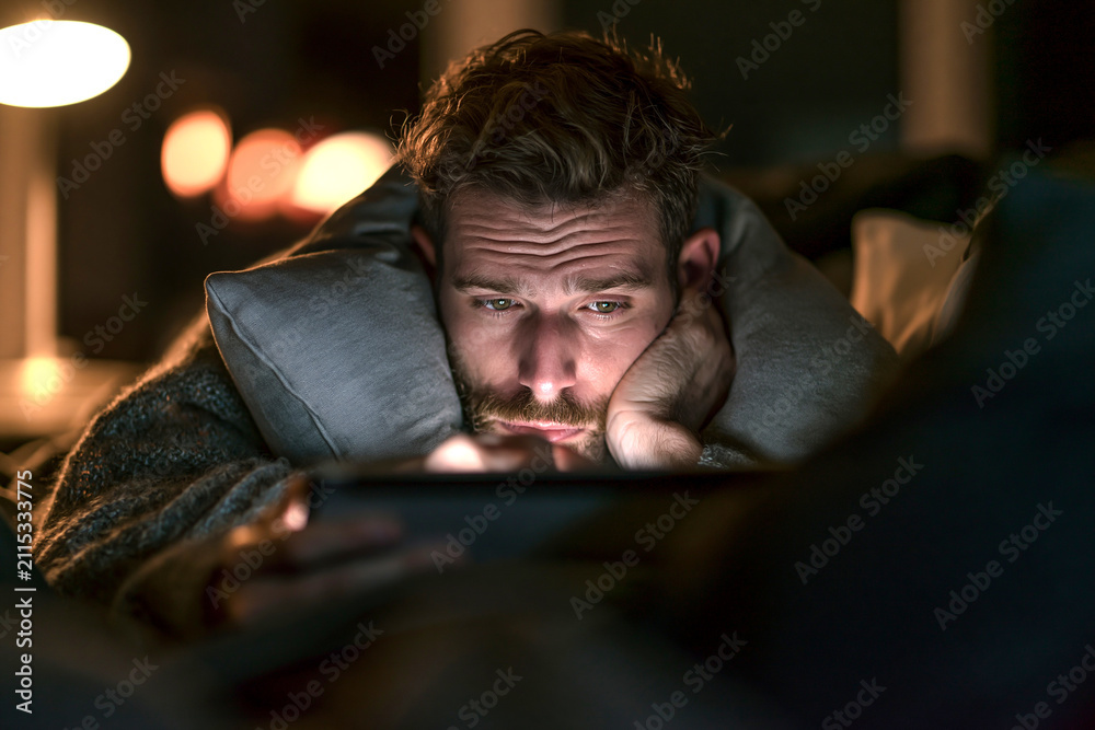 Obraz premium 夜の部屋で頬杖をつきながらタブレットを見る男性
