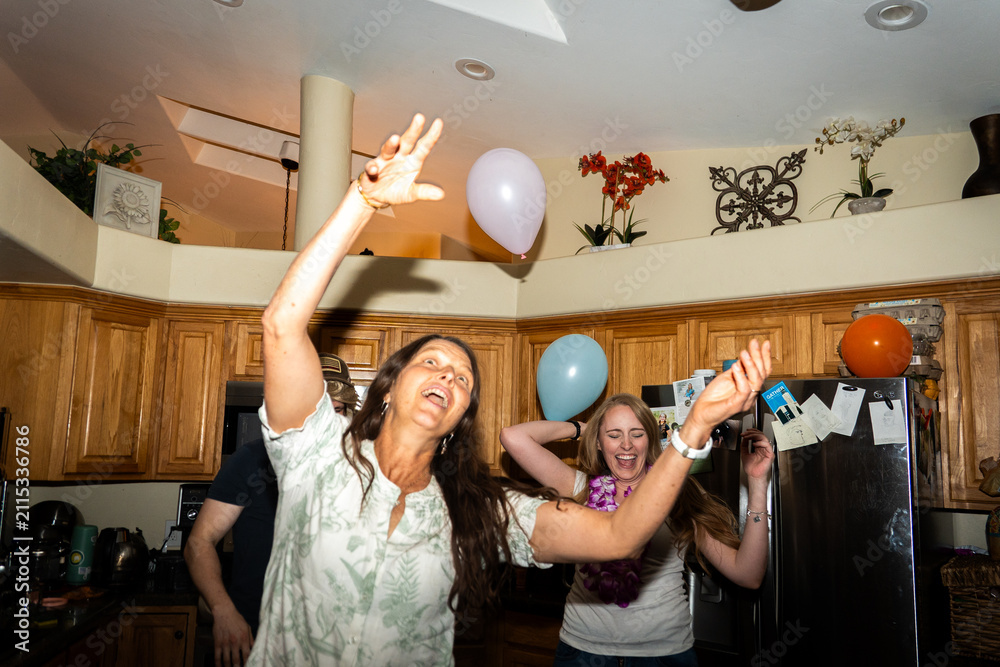 Naklejka premium Indoor celebration with balloons, raised hands, cheerful kitchen gathering
