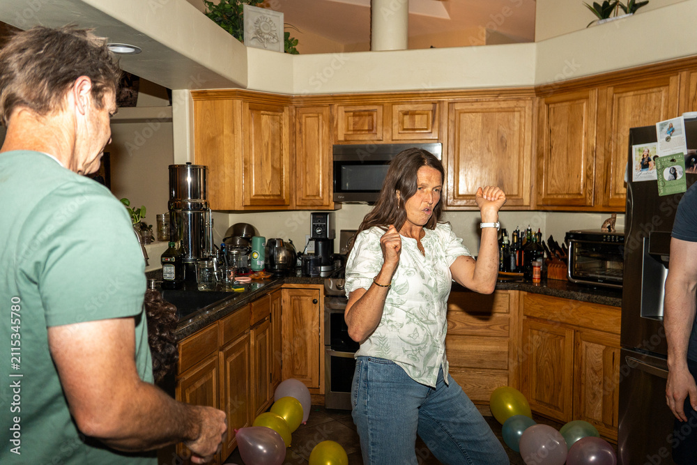 Naklejka premium Adults dancing in kitchen during lively home celebration with balloons