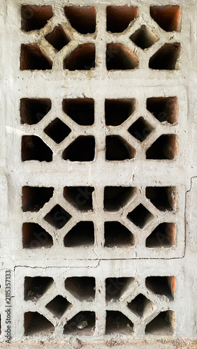 Vertical composition of aged concrete ventilation blocks with geometric openings and exposed clay bricks. Rustic architectural detail creating a repeating abstract pattern for background use.