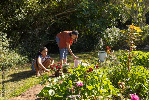 African American mother and teen daughter watering potted plants in backyard with pink watering can