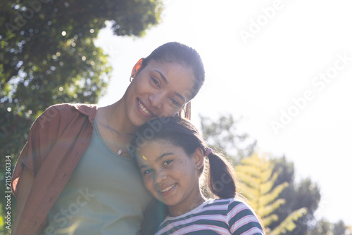 African American mother and teenage daughter leaning into camera in park wearing tank top, pendant