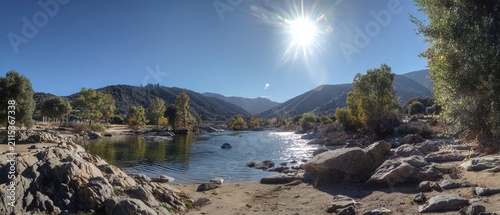 Scenic River Landscape with Rocks, Trees, and Bright Sunlight.