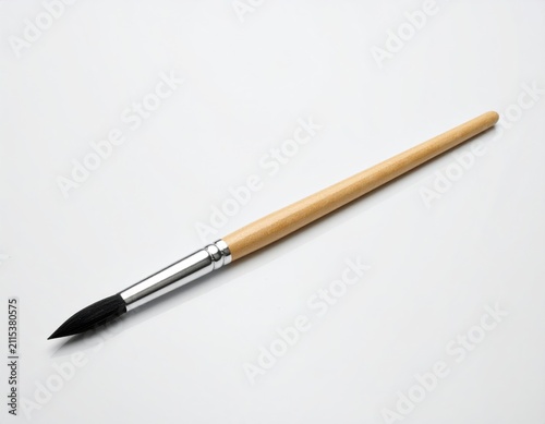 A single, pointed, fine-tipped brush with a wooden handle and silver ferrule rests on a white surface
