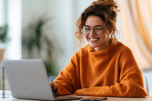 Happy young woman using laptop sitting at desk writing notes while watching webinar, studying online, looking at pc screen learning web classes or having virtual call meeting remote working from home.