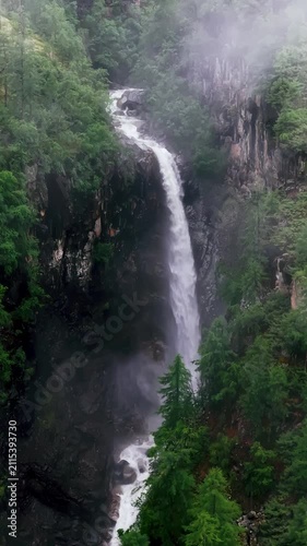 Majestic waterfall in misty mountains with coniferous forest. Vertical 9:16 footage perfect for travel vlogs, meditation apps, social media stories, and nature documentaries. Cinematic and atmospheric