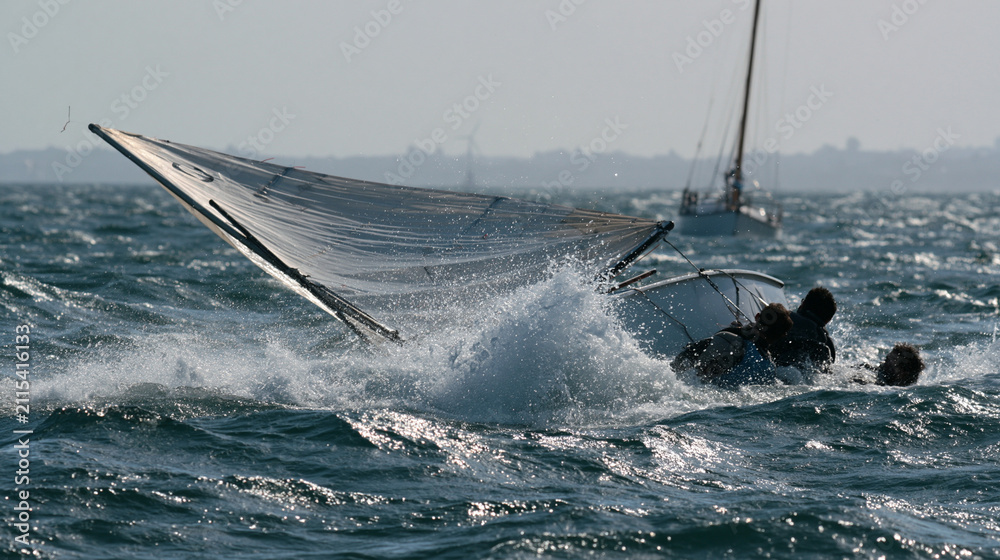 Obraz premium Sailing boat racing on azure waters with surging waves and tilted sail in a rescue operation scenario
