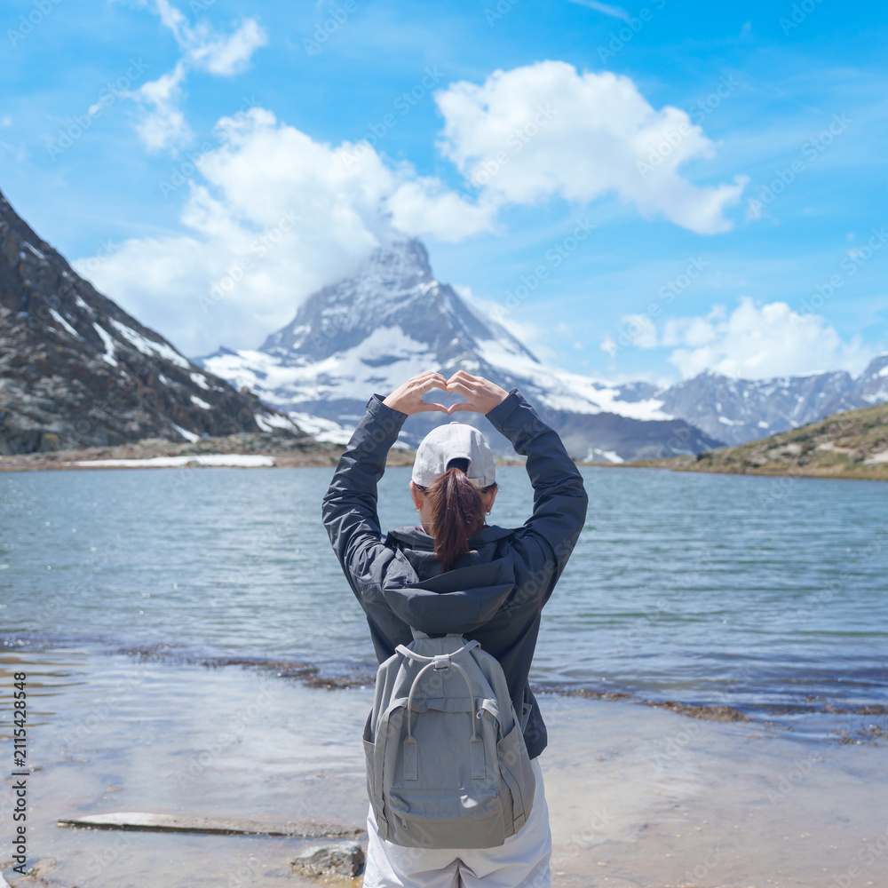 Fototapeta premium Woman Tourist Exploring Zermatt, Switzerland. Traveler Making Heart Shape with Hands at Riffelsee Lake and Matterhorn, Famous European Landmark, Hiking Attraction, Travel Destination in Europe