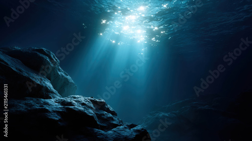 Sunlight streams through the dark blue ocean water, illuminating the seabed and a rocky formation. The light creates a mystical and serene atmosphere.
