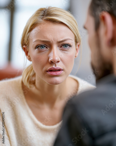 A woman with a serious expression listens intently to a man in a close, emotional conversation indoors.