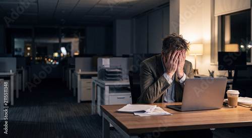 Exhausted businessman covering face at desk in dark late night office, Chicago, Illinois, USA, North America