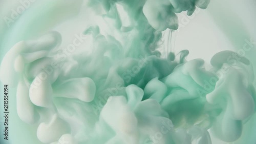 Watercolor pigment blooms through clear water as soft sage green and ivory hues unfurl into organic cloudlike formations under gentle overhead lighting with elegant cinematic macro motion.