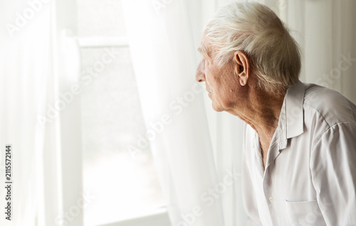 an elderly  gray-haired man looks out the window