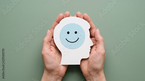 Hands holding a human head silhouette paper cutout with a blue smiling face icon symbolizing positive mental health