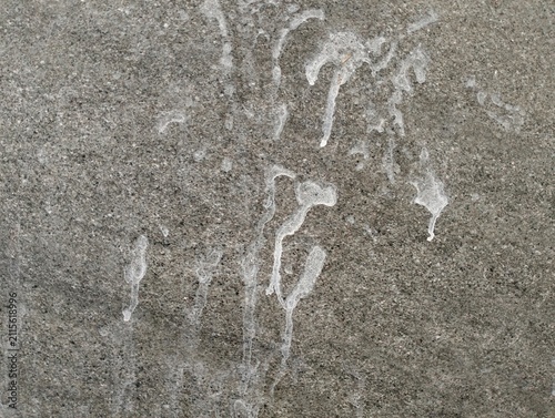 Abstract white mineral efflorescence stains and water drippings on dark grey stone surface texture background for design overlay.